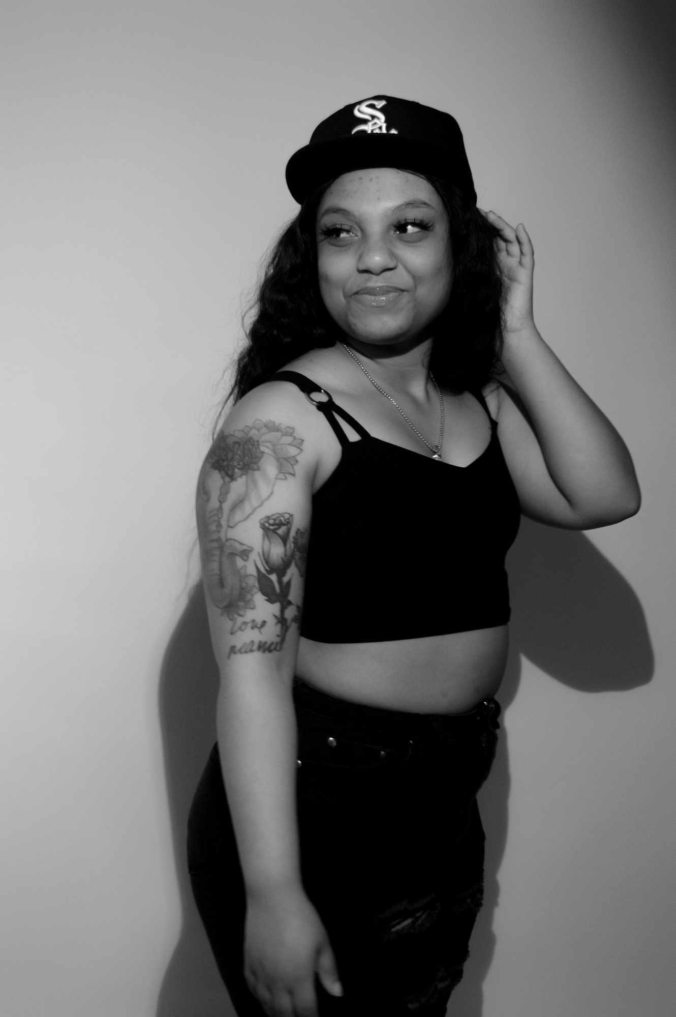 Black and white image of a black female wearing a hat, standing and looking off to the side with a tattoo on her right arm.